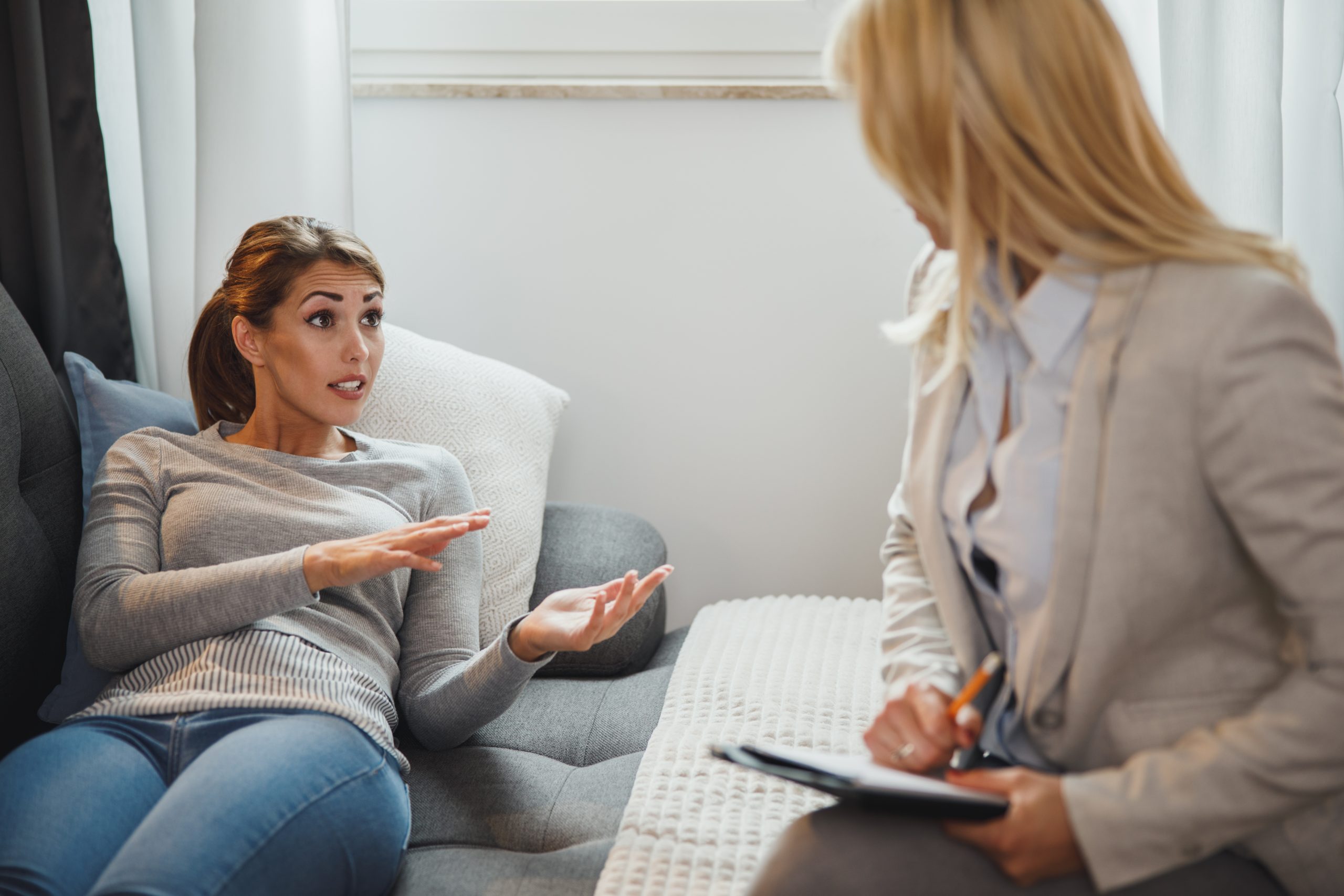 Shot of a stressed out young woman having a discussion with her female psychotherapist while being seated on a sofa inside of a living room.