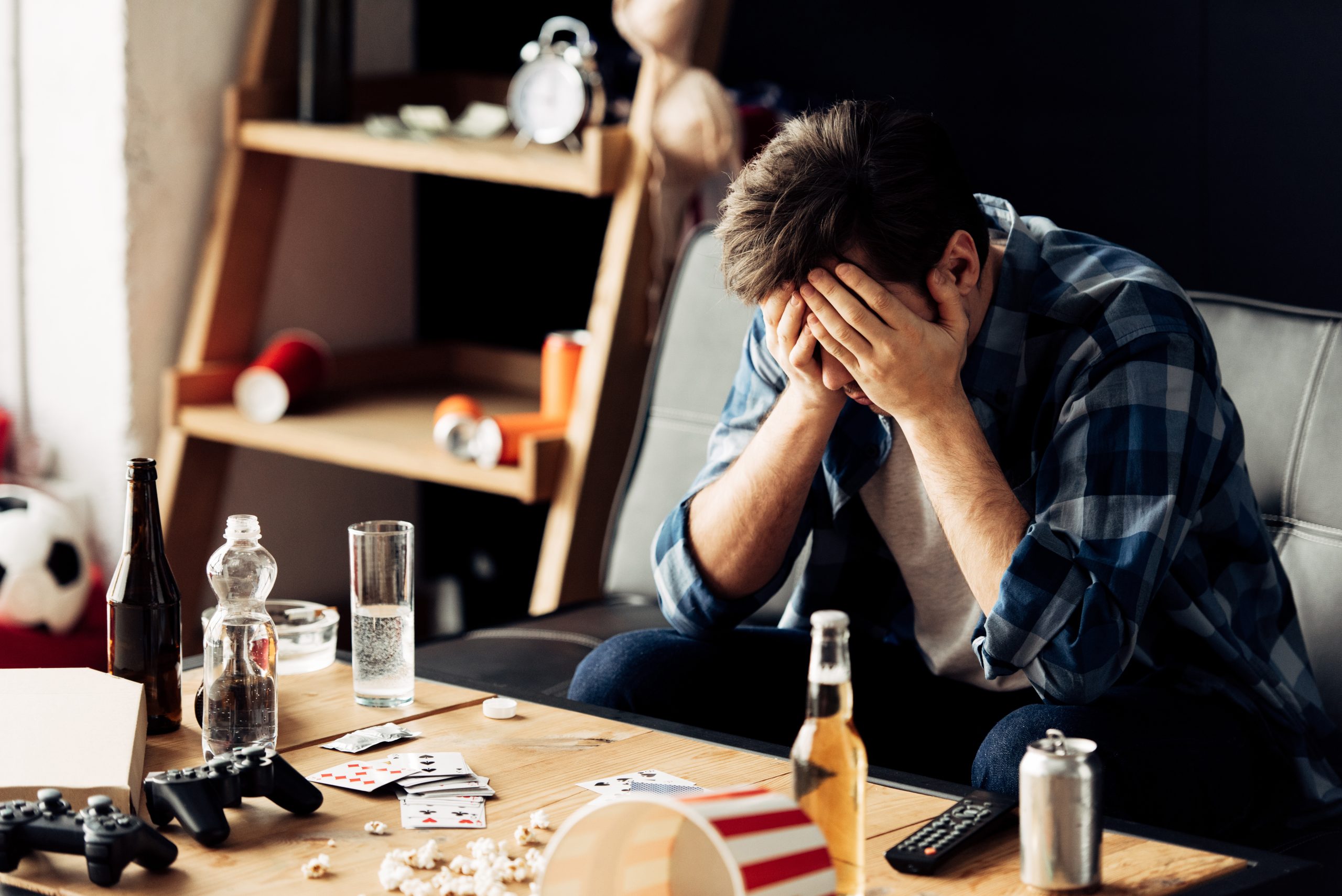 handsome man suffering from hangover holding hand while sitting near coffee table